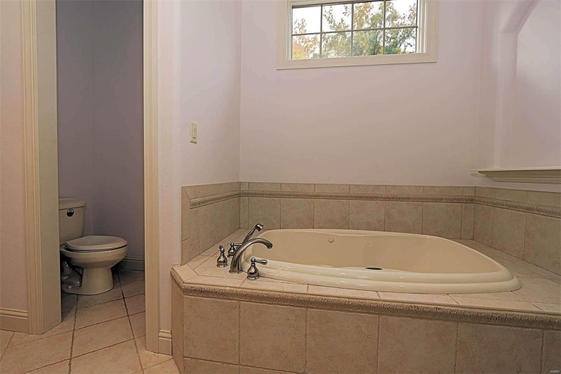 Bathroom with tiled bath, toilet, and tile patterned floors