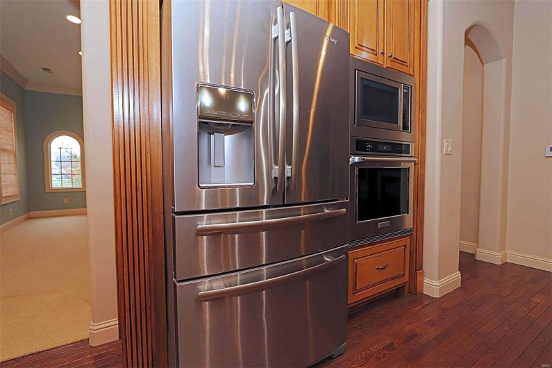 Kitchen with ornamental molding, dark wood-type flooring, appliances with stainless steel finishes, and decorative columns