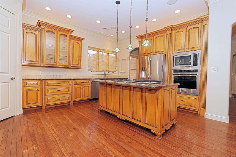 Kitchen featuring appliances with stainless steel finishes, wood-type flooring, a center island, ornamental molding, and decorative light fixtures