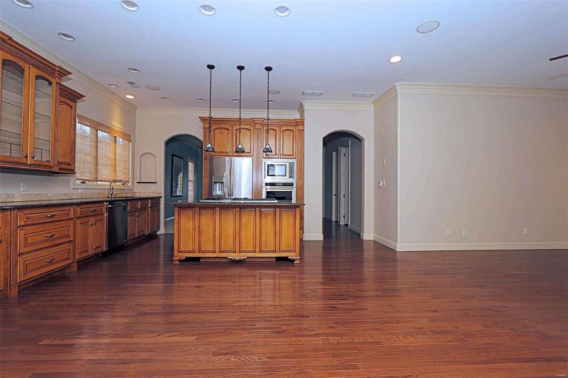 Kitchen featuring dark wood-type flooring, stainless steel appliances, ornamental molding, and hanging light fixtures