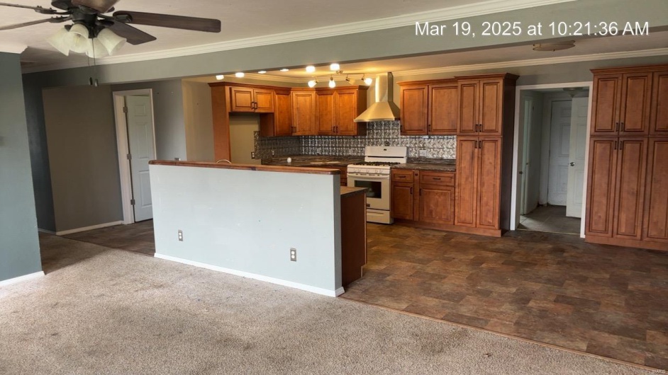 Kitchen with wall chimney exhaust hood, a ceiling fan, white gas stove, and brown cabinetry