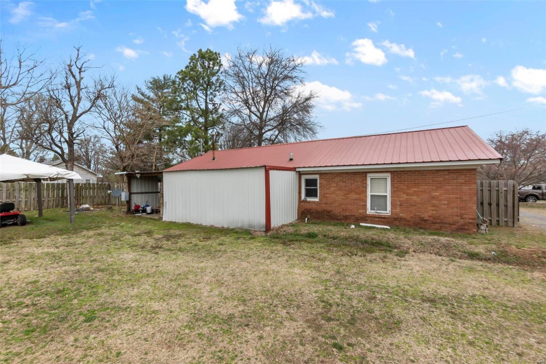 Back of property with brick siding, fence, a lawn, and metal roof