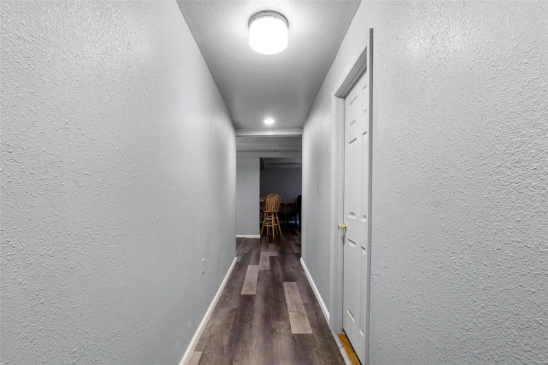 Hall featuring wood finished floors, a textured wall, baseboards, and a textured ceiling