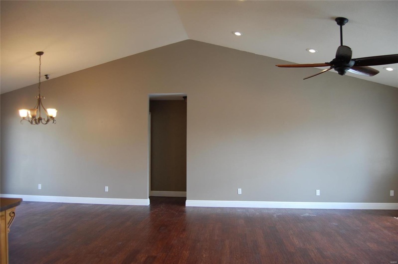Spare room featuring lofted ceiling, ceiling fan with notable chandelier, dark wood-type flooring, and baseboards