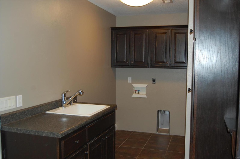 Laundry area with electric dryer hookup, dark tile patterned flooring, a sink, cabinet space, and hookup for a washing machine