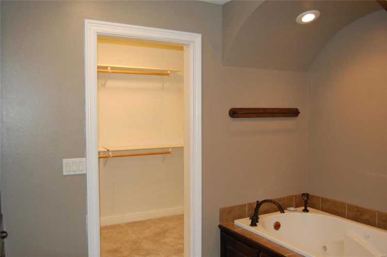 Bathroom with a spacious closet, recessed lighting, a tub with jets, and baseboards