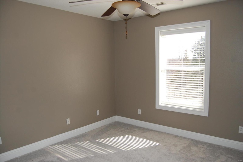 Empty room featuring a wealth of natural light, light carpet, baseboards, and ceiling fan