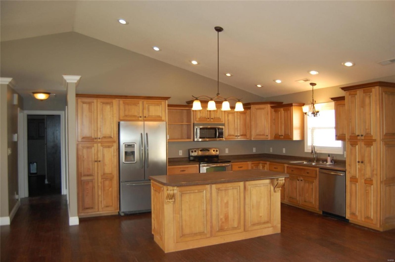 Kitchen with dark countertops, a center island, vaulted ceiling, appliances with stainless steel finishes, and a sink