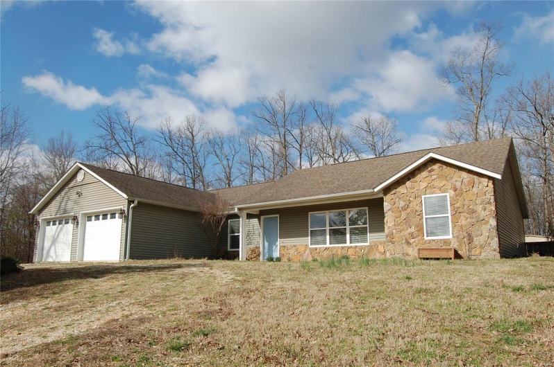 Ranch-style home featuring stone siding, an attached garage, a front yard, and roof with shingles