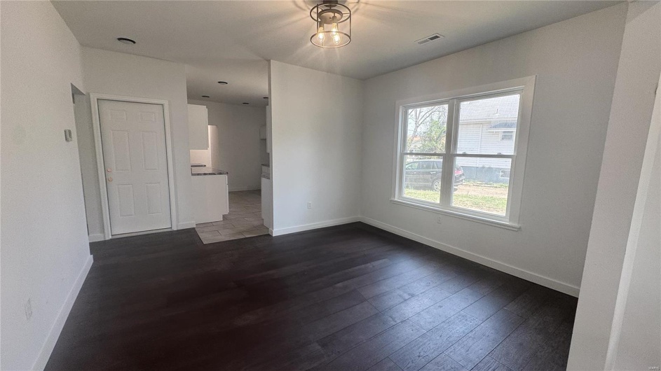 Empty room with dark wood-type flooring, baseboards, and visible vents