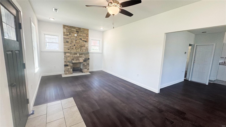 Unfurnished living room with baseboards, ceiling fan, visible vents, a fireplace, and wood finished floors