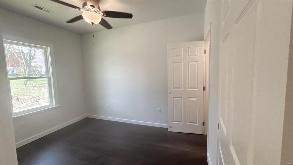 Empty room with dark wood finished floors, baseboards, visible vents, and a ceiling fan