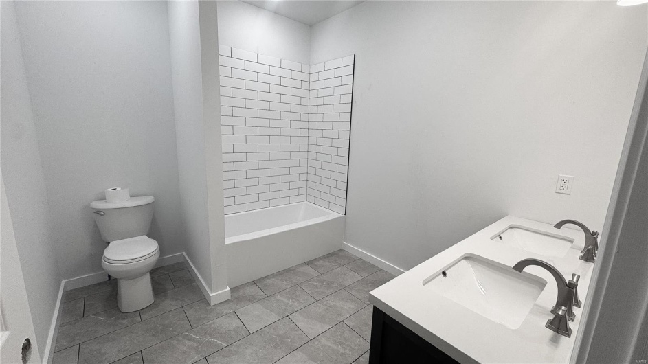 Full bathroom with toilet, a sink, double vanity, and baseboards