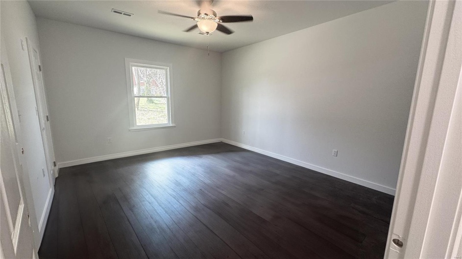 Unfurnished room with baseboards, dark wood-style flooring, ceiling fan, and visible vents