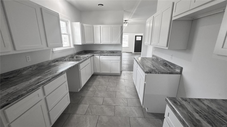 Kitchen with a healthy amount of sunlight, white cabinetry, a sink, and dark stone counters
