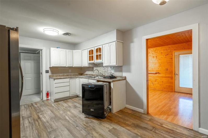 Kitchen with light wood-style flooring, freestanding refrigerator, white cabinets, dishwasher, and backsplash