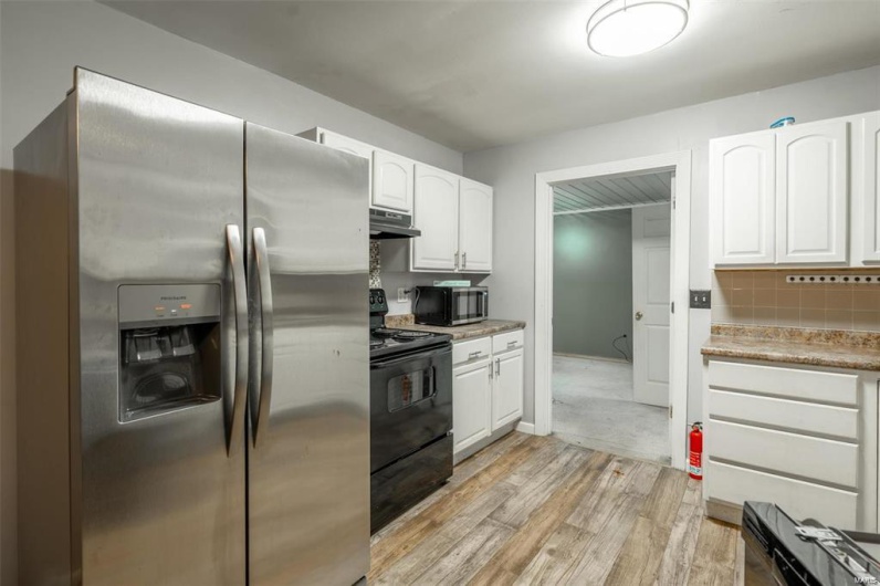 Kitchen featuring light wood-style flooring, under cabinet range hood, white cabinetry, appliances with stainless steel finishes, and decorative backsplash