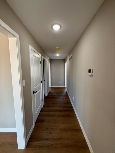 Corridor with dark wood finished floors, visible vents, and baseboards