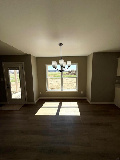 Unfurnished dining area featuring dark wood finished floors, an inviting chandelier, a healthy amount of sunlight, and baseboards