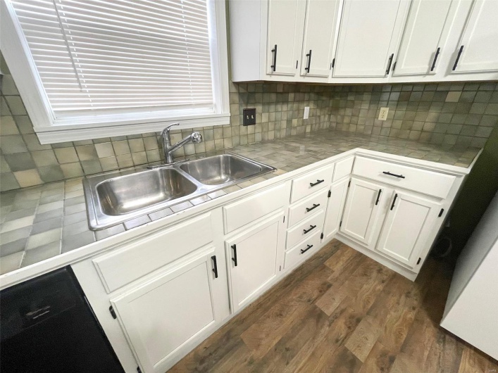 Kitchen with tasteful backsplash, dark wood-type flooring, sink, white cabinets, and tile counters