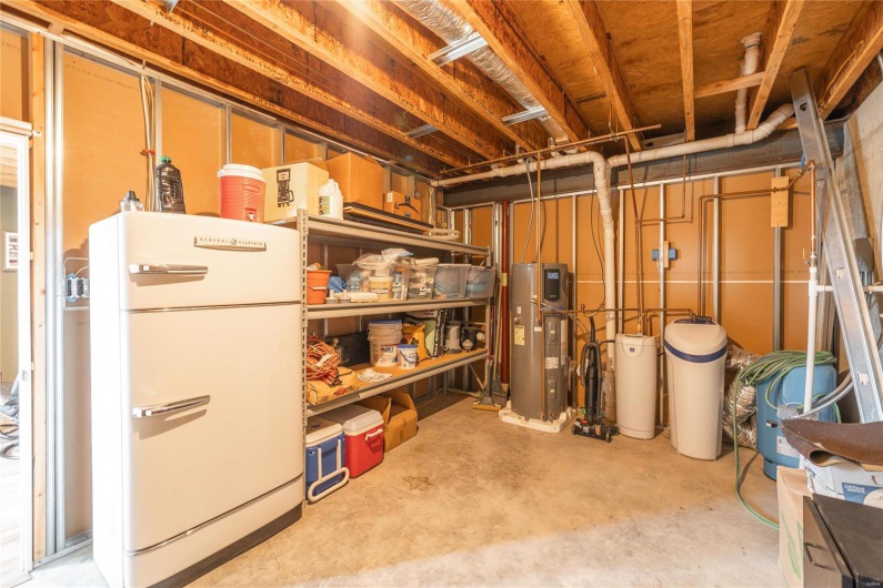 Unfinished below grade area featuring water heater and freestanding refrigerator