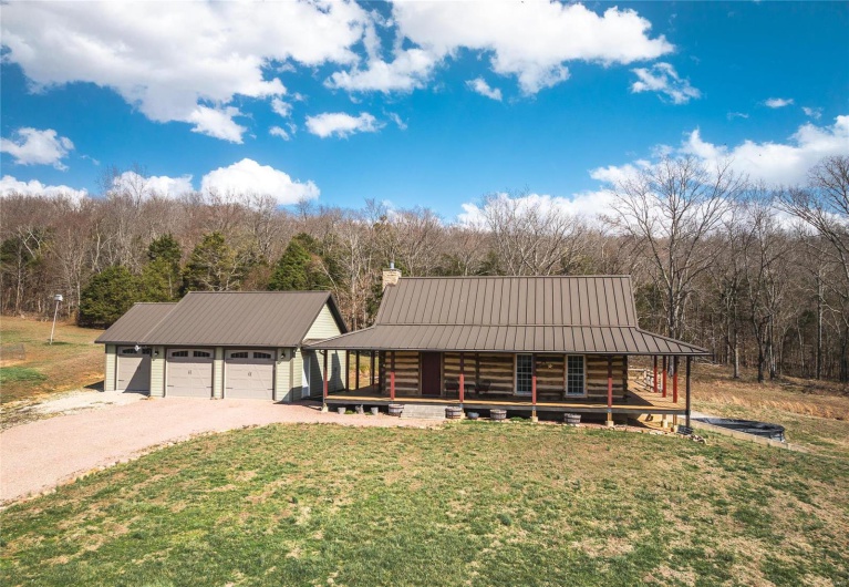 View of front facade featuring metal roof, a front lawn, covered porch, and dirt driveway