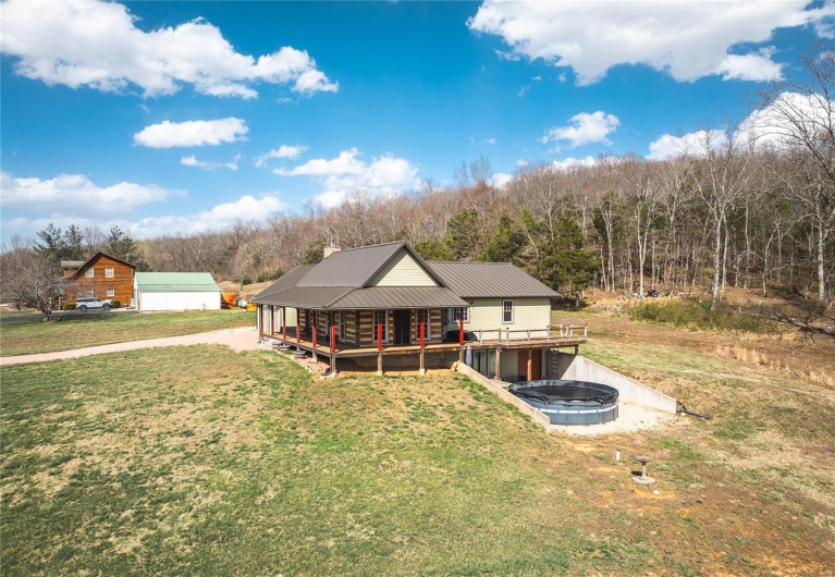 Rear view of house with a lawn, driveway, metal roof, and a deck