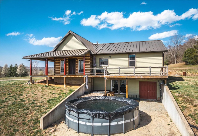 Rear view of house featuring a wooden deck, a standing seam roof, a covered pool, an attached garage, and metal roof