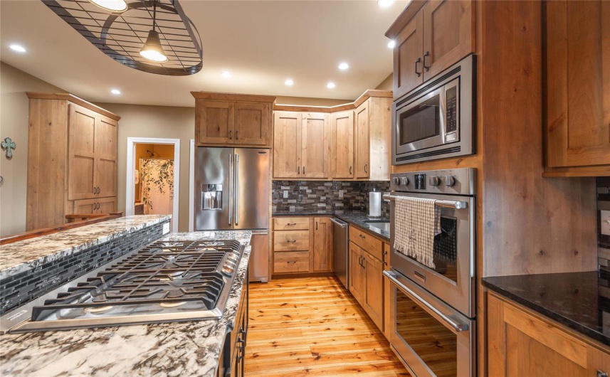 Kitchen with dark stone countertops, backsplash, recessed lighting, light wood-style floors, and appliances with stainless steel finishes
