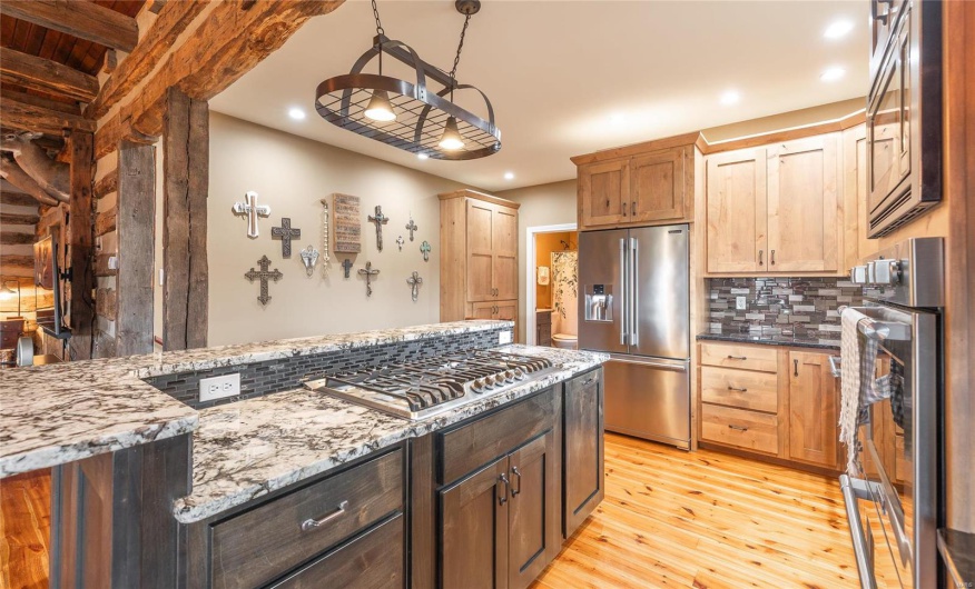 Kitchen featuring light stone countertops, hanging light fixtures, light wood-style floors, appliances with stainless steel finishes, and tasteful backsplash