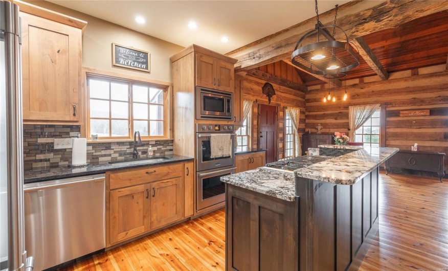 Kitchen featuring wooden walls, light wood-type flooring, beam ceiling, stainless steel appliances, and a sink
