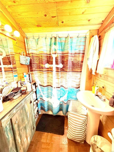 Bathroom with a sink, wood walls, wooden ceiling, and a shower with curtain