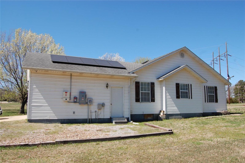 Back of house with roof mounted solar panels, roof with shingles, entry steps, and a yard