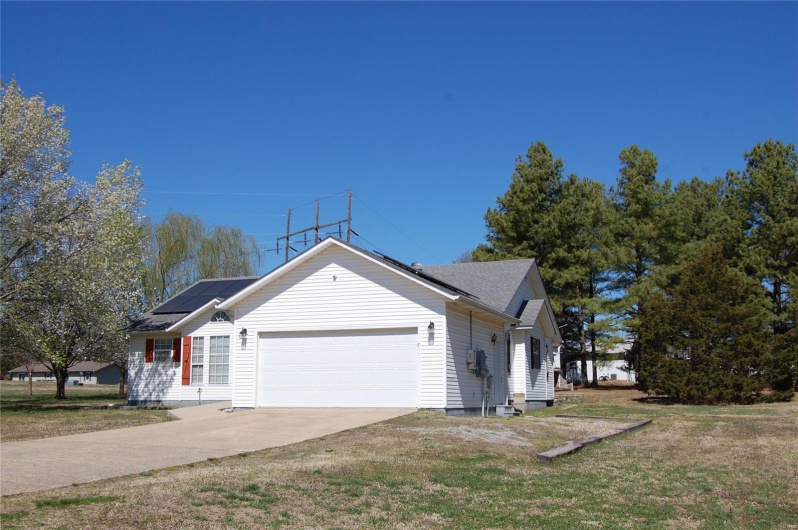 View of side of home featuring solar panels, an attached garage, concrete driveway, and a yard