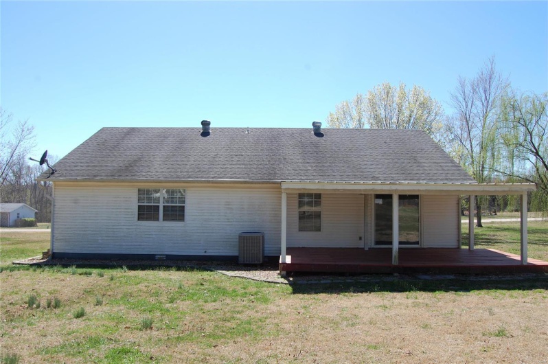 Rear view of house with a deck, roof with shingles, and a lawn