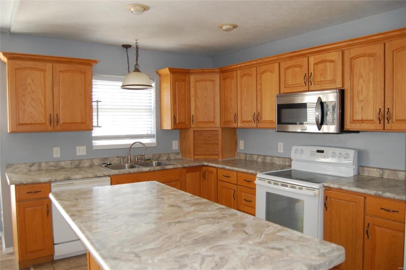 Kitchen with light countertops, white appliances, a sink, hanging light fixtures, and a center island