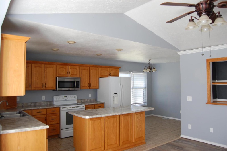 Kitchen with vaulted ceiling, a sink, ceiling fan with notable chandelier, a center island, and white appliances