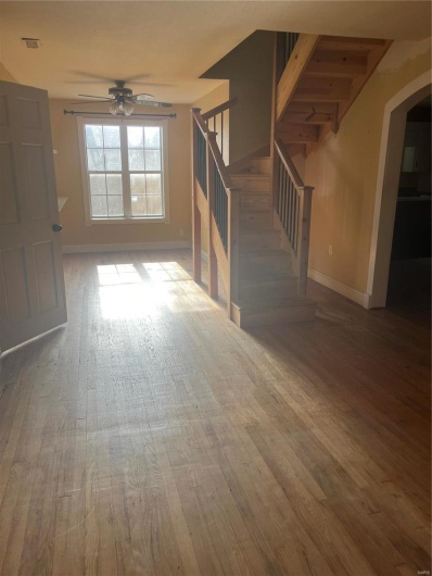 Unfurnished living room with stairs, baseboards, arched walkways, ceiling fan, and wood finished floors