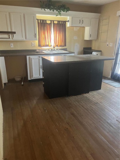 Kitchen with white cabinets, dark countertops, a kitchen island, and dark wood finished floors