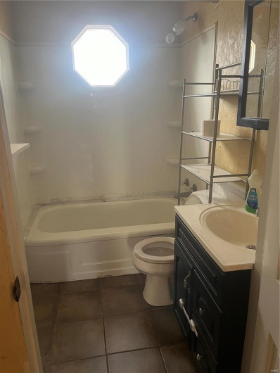 Bathroom with shower / bathing tub combination, toilet, tile patterned flooring, and vanity