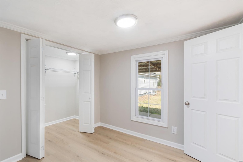 Unfurnished bedroom featuring crown molding, baseboards, a closet, and light wood-style flooring