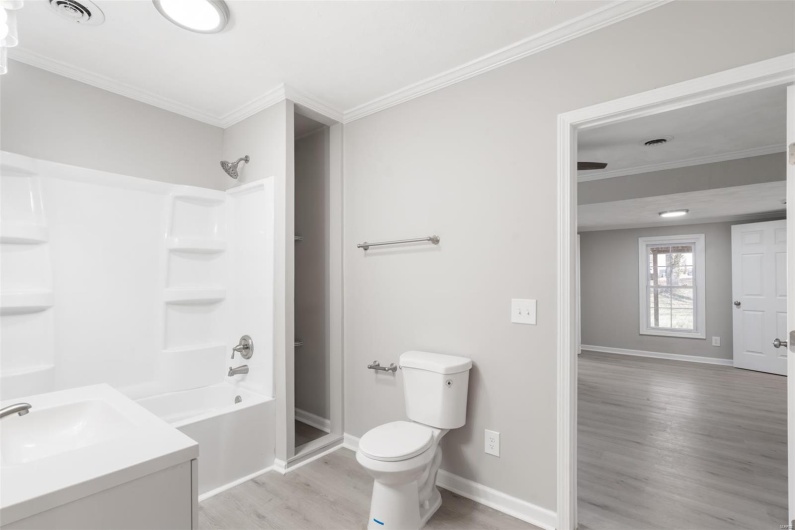 Full bathroom with crown molding, toilet, wood finished floors, baseboards, and visible vents