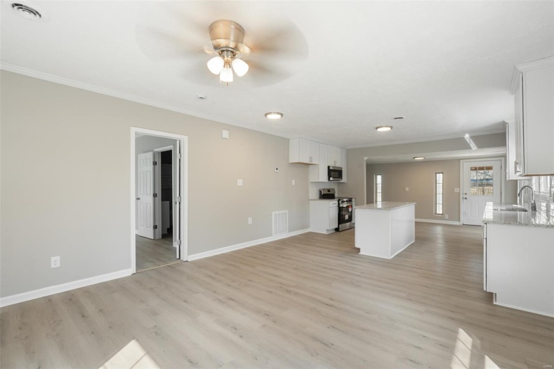 Unfurnished living room with crown molding, baseboards, a sink, light wood finished floors, and a ceiling fan