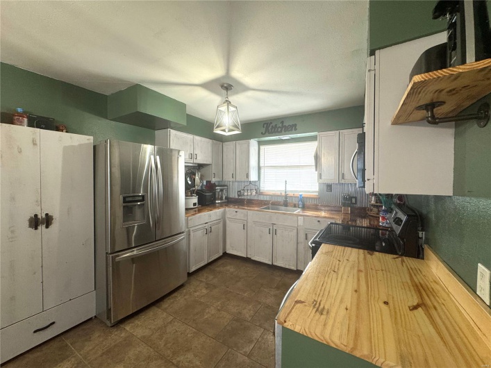 Kitchen with butcher block counters, appliances with stainless steel finishes, white cabinetry, a sink, and decorative light fixtures