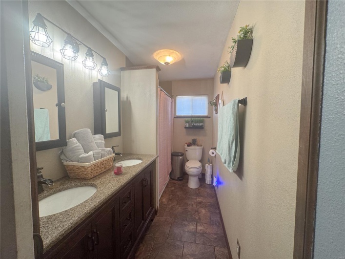 Bathroom with toilet, a sink, stone finish floor, and double vanity