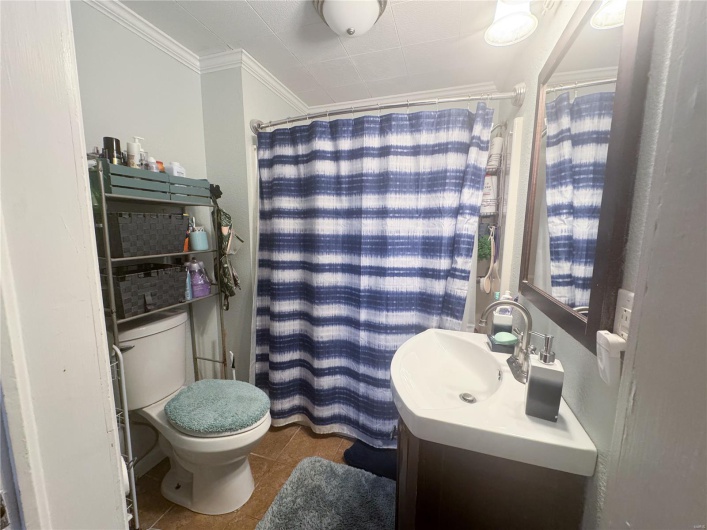 Full bath with tile patterned flooring, vanity, toilet, ornamental molding, and a shower with shower curtain