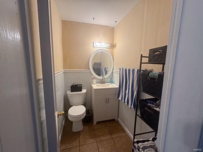 Bathroom with toilet, vanity, wainscoting, tile patterned flooring, and tile walls