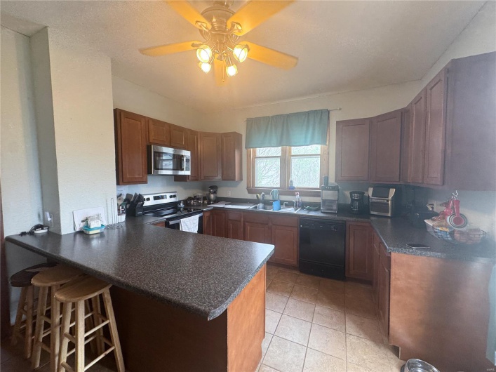 Kitchen with a kitchen bar, stainless steel appliances, light tile patterned flooring, dark countertops, and a peninsula