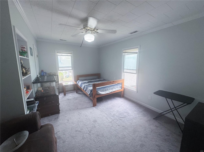 Carpeted bedroom featuring baseboards, visible vents, ceiling fan, and ornamental molding