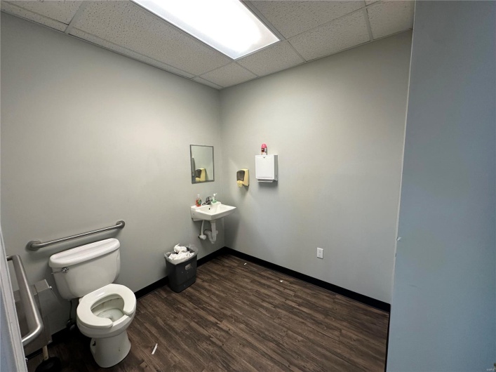 Half bathroom featuring a drop ceiling, baseboards, toilet, and wood finished floors